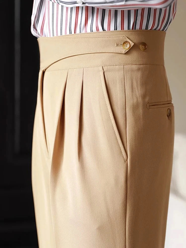 Beige pleated pants with gold buttons worn by a person, with a blurred background.