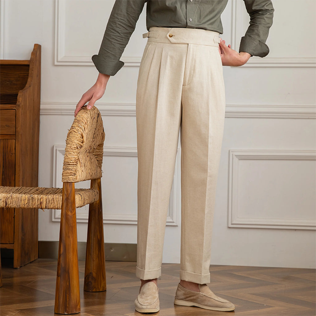 Person wearing beige pants and a green shirt standing next to a wooden chair in an elegant room.