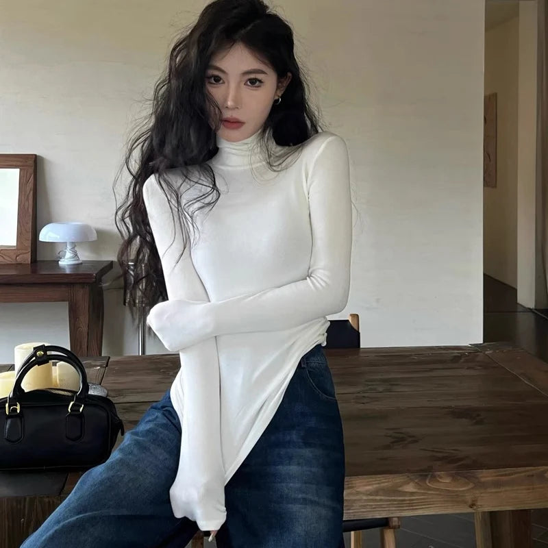 Woman wearing a white turtleneck and blue jeans sitting on a wooden table.