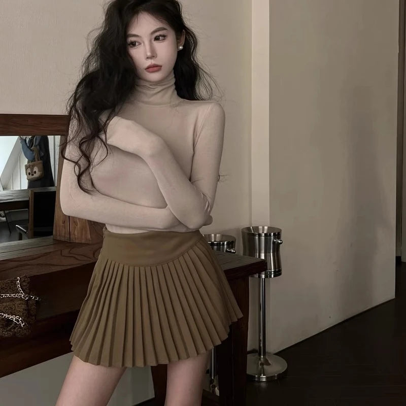 Woman wearing a beige turtleneck and pleated skirt in an indoor setting